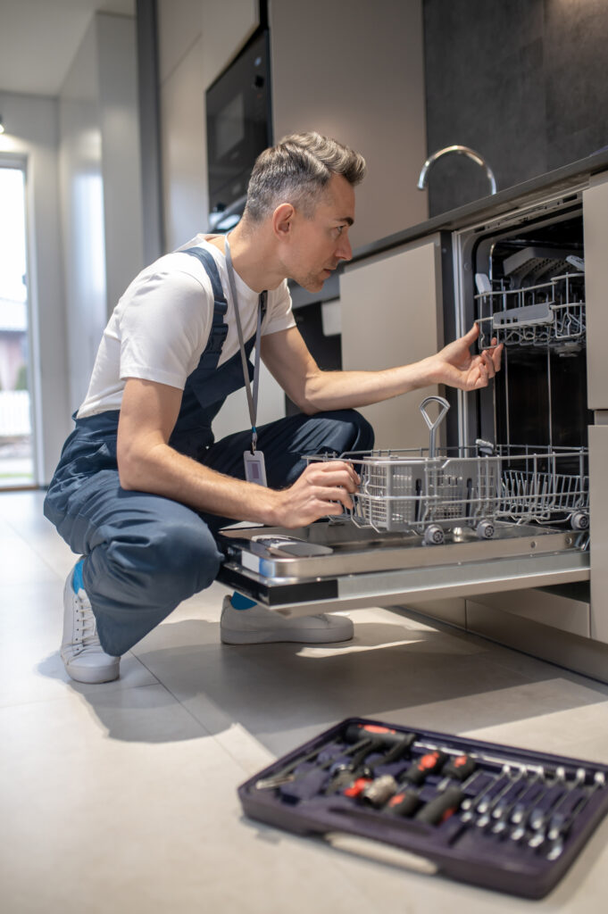 profile of man crouching looking into open dishwasher